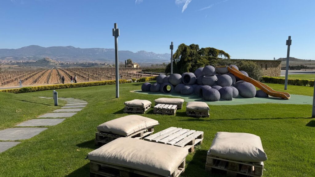 Lawn at Vivanco in Rioja with seating area and grape-themed slide with fields in the background