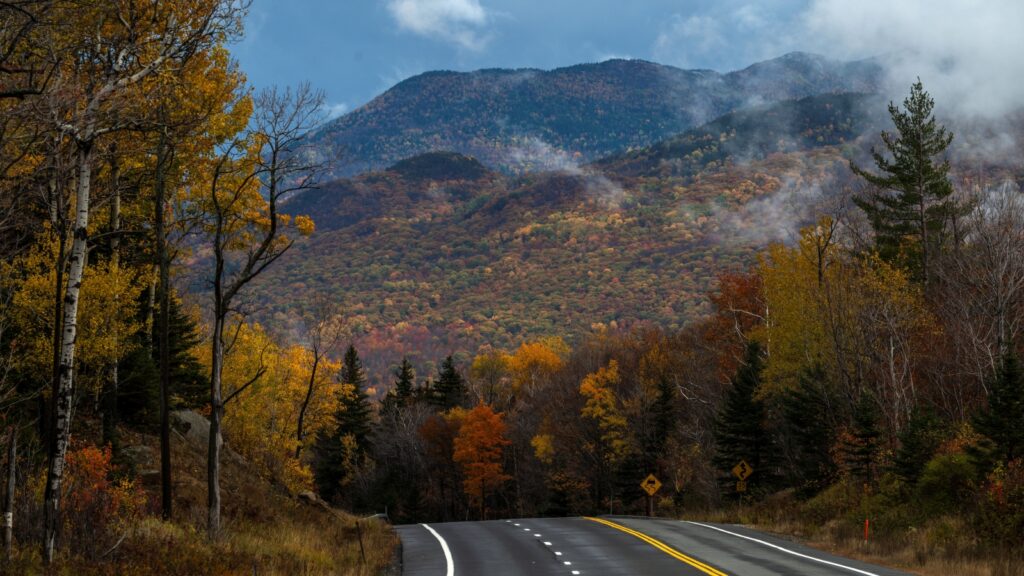 A road surrounded by fall foliage and mountains in The Adirondacks