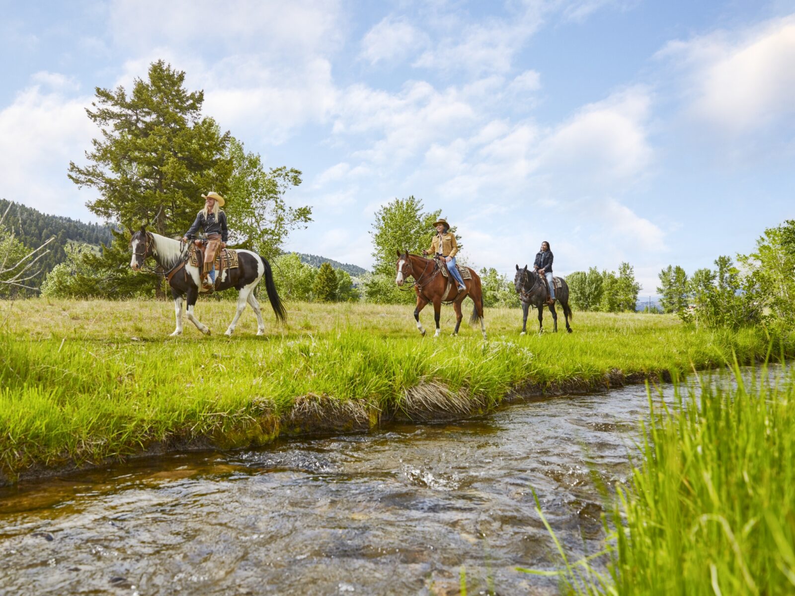 Three horseback riders by a stream at The Ranch at Rock Creek