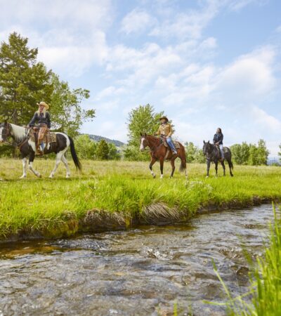 Three horseback riders by a stream at The Ranch at Rock Creek